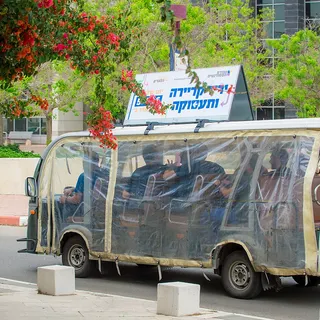 אוטובוס מינית עם כיסוי פלסטיק, נוסעים ופרחים, נוסע לאורך כביש עירוני.